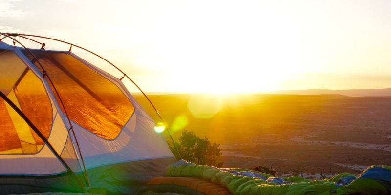 orange tent camped at sunrise with sleeping bags outside